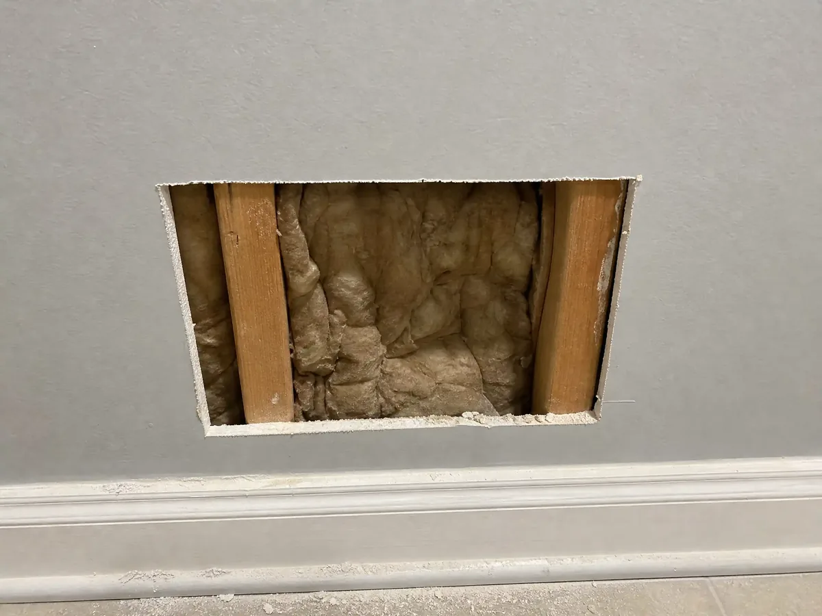 Hands cutting out the damaged water-stained drywall section with a drywall saw along a marked rectangle